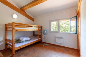 Um quarto com uma cama de solteiro em madeira, um ventilador, uma janela com vista para árvores e um radiador branco.