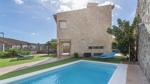 Une piscine avec des chaises longues, un bâtiment en pierre et un ciel dégagé.