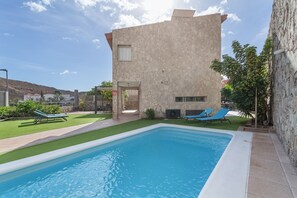 A swimming pool with lounge chairs, a stone building, and a clear sky.