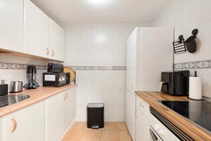 Una cocina compacta con armarios blancos, una cafetera, un tostador y un cubo de basura.