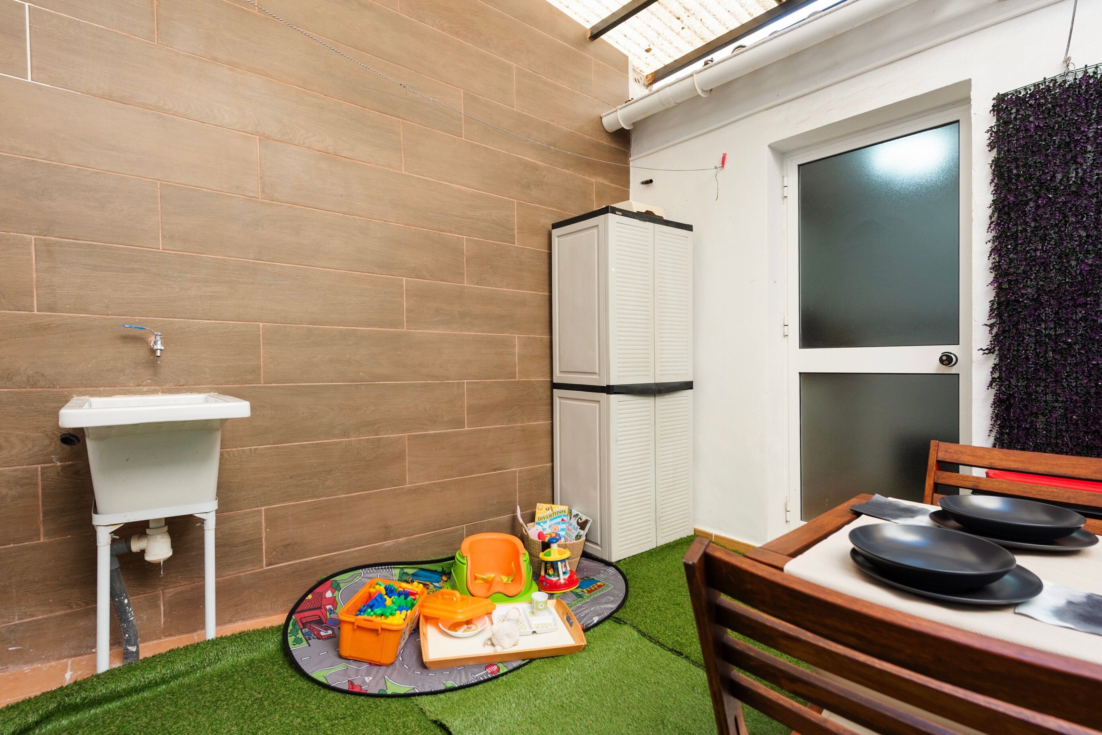 Een kleine kamer met een wastafel, een kleine koelkast, een deur met ruitverdeling en een zithoek met een tafel en stoelen.