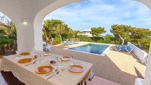 A dining area with a table set for six, overlooking a pool and a villa.