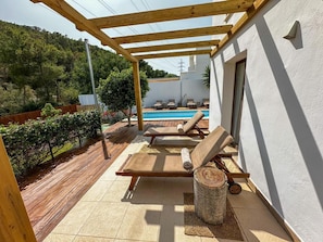 A covered outdoor area with a pool, lounge chairs, and a pergola.