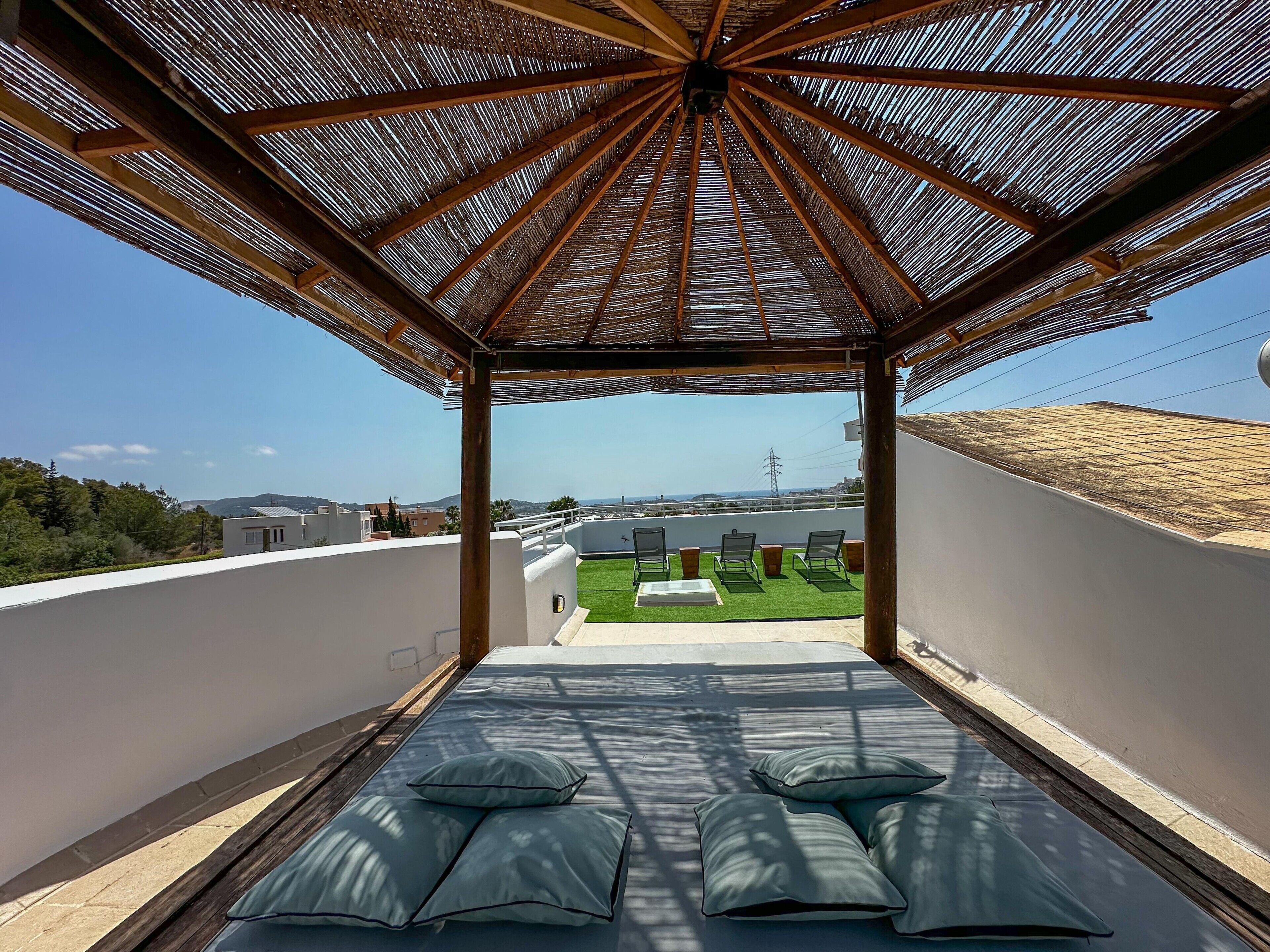 A covered outdoor seating area with a view of a green lawn and distant buildings.