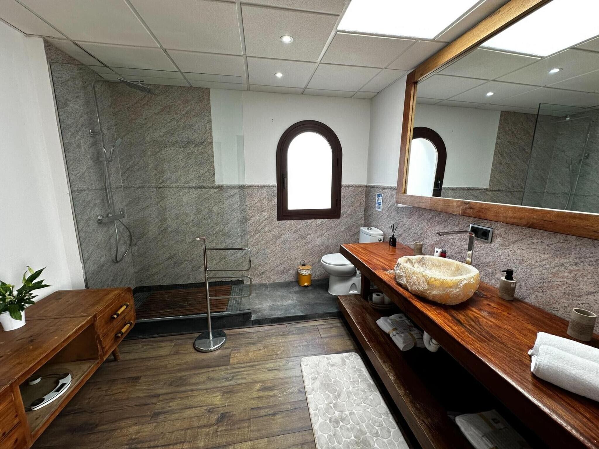 Een moderne badkamer met een houten wastafelmeubel, een grote spiegel, een douche en een marmeren wand.