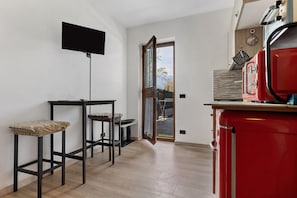 A room with a TV mounted on the wall, a red appliance, and a door leading outside.
