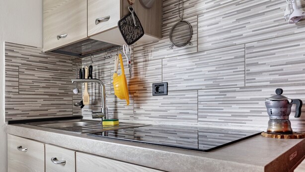Et køkken med moderne design, komplet med en stribet backsplash, en stålvask og forskellige redskaber hængende på væggen.
