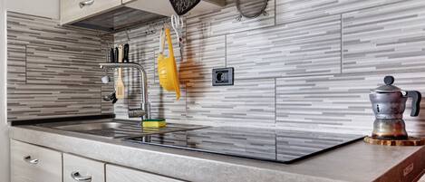 A kitchen with a modern design, featuring a striped backsplash, a stainless steel sink, and various utensils hanging on the wall.