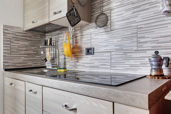 Una cocina de diseño moderno, con un salpicadero a rayas, un lavamanos de acero inoxidable y diversos utensilios colgados en la pared.