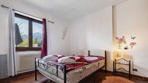 En enkeltseng med metalramme, et vindue med gardiner, en radiator, en blød måtte og vægdekorationer med blomster og sommerfugle.