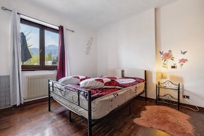 Una cama individual con estructura metálica, una ventana con cortinas, un radiador, una alfombra mullida y adornos en la pared que incluyen flores y mariposas.