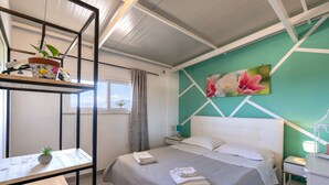 Un dormitorio con cama, mesitas de noche, escritorio, planta en maceta y ventana con cortinas.