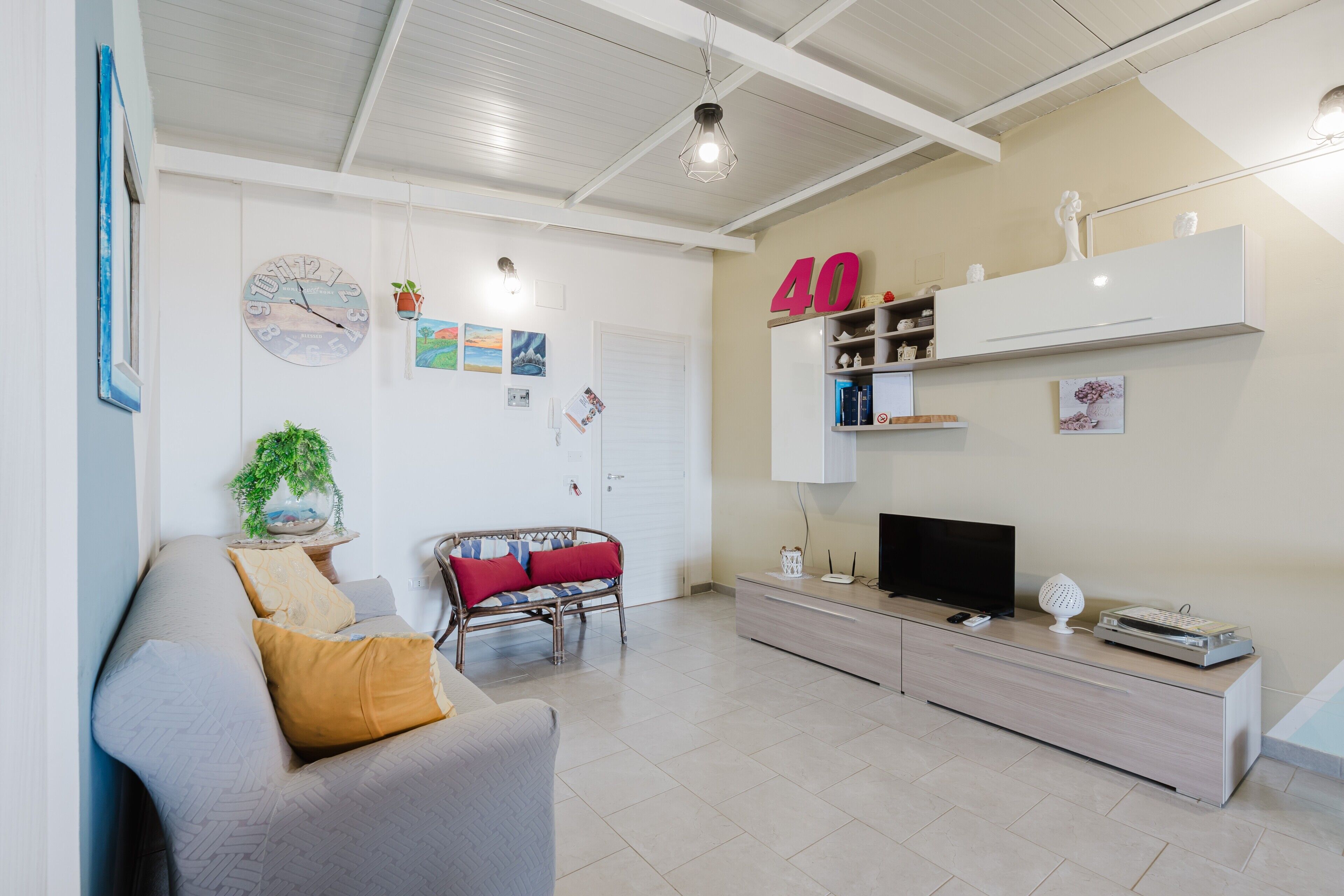 A living room with a sofa, a television, a wall clock, and a shelf with decorative items.