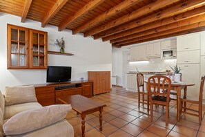 Uma sala de estar com sofá, televisão, armário de madeira e um espaço de jantar com cadeiras e mesa.