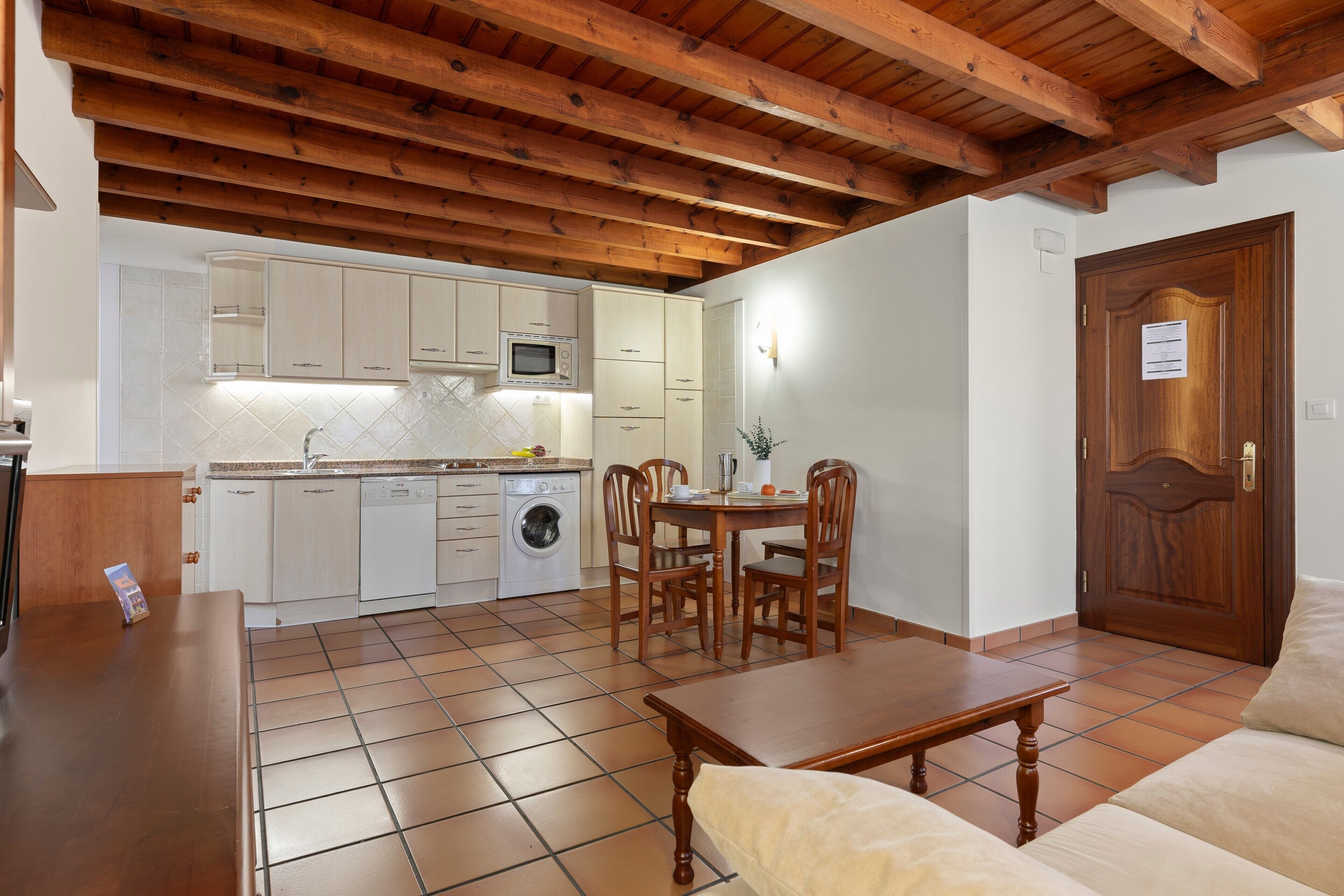 Een keuken met witte kastjes, een houten eettafel en een houten plafond.