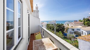 A balcony with a wooden table and chairs, a view of the sea, and buildings in the background.