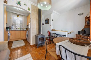 A kitchen with a wood-burning stove, a dining area with a table and chairs, and a view of the living room.
