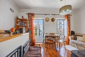 Ein gemütlicher Wohnbereich mit Holztisch, Stühlen, einer Couch, einem Bücherregal und Blick durch eine Glastür.