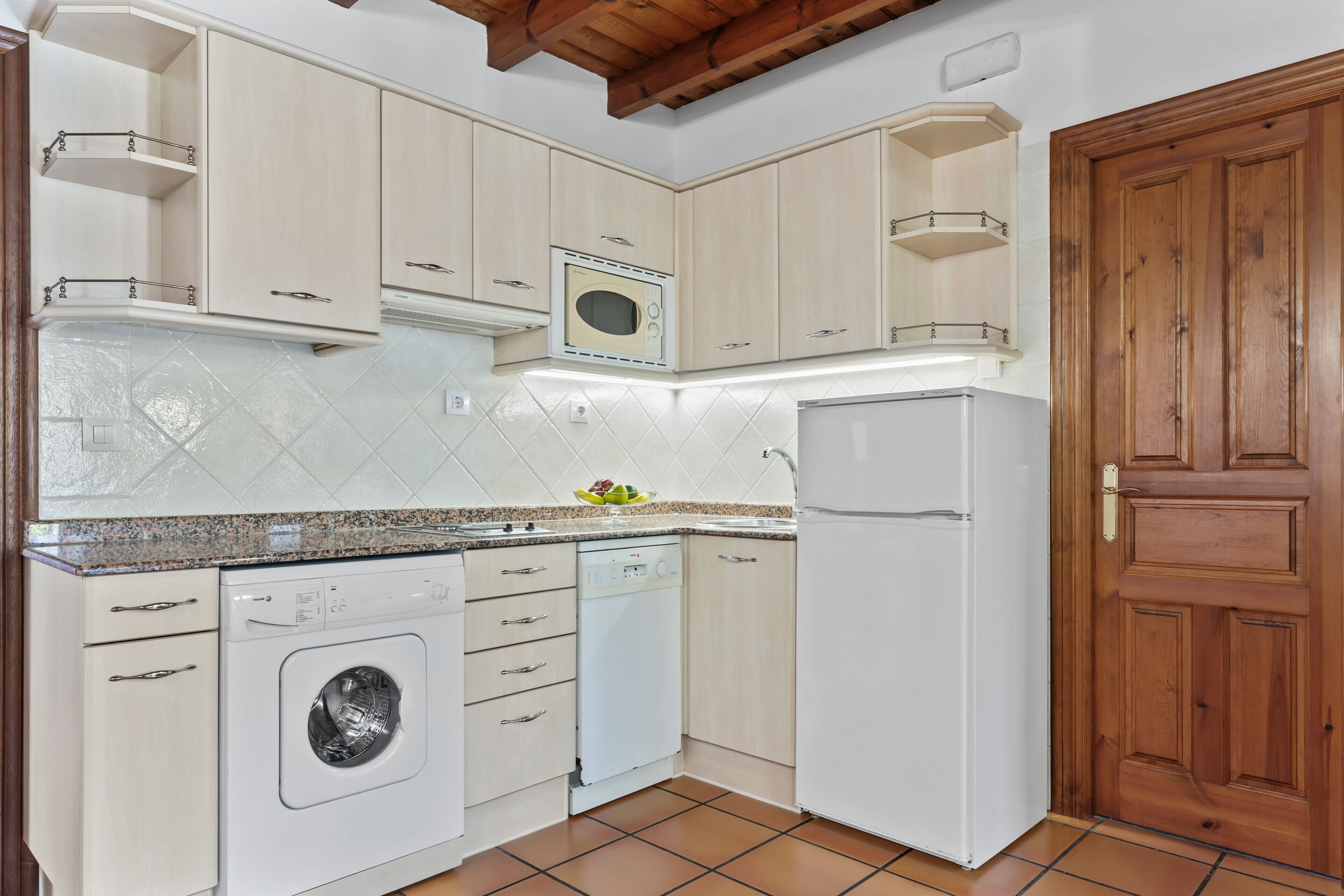 A kitchen with a washing machine, dishwasher, microwave, and a wooden door.
