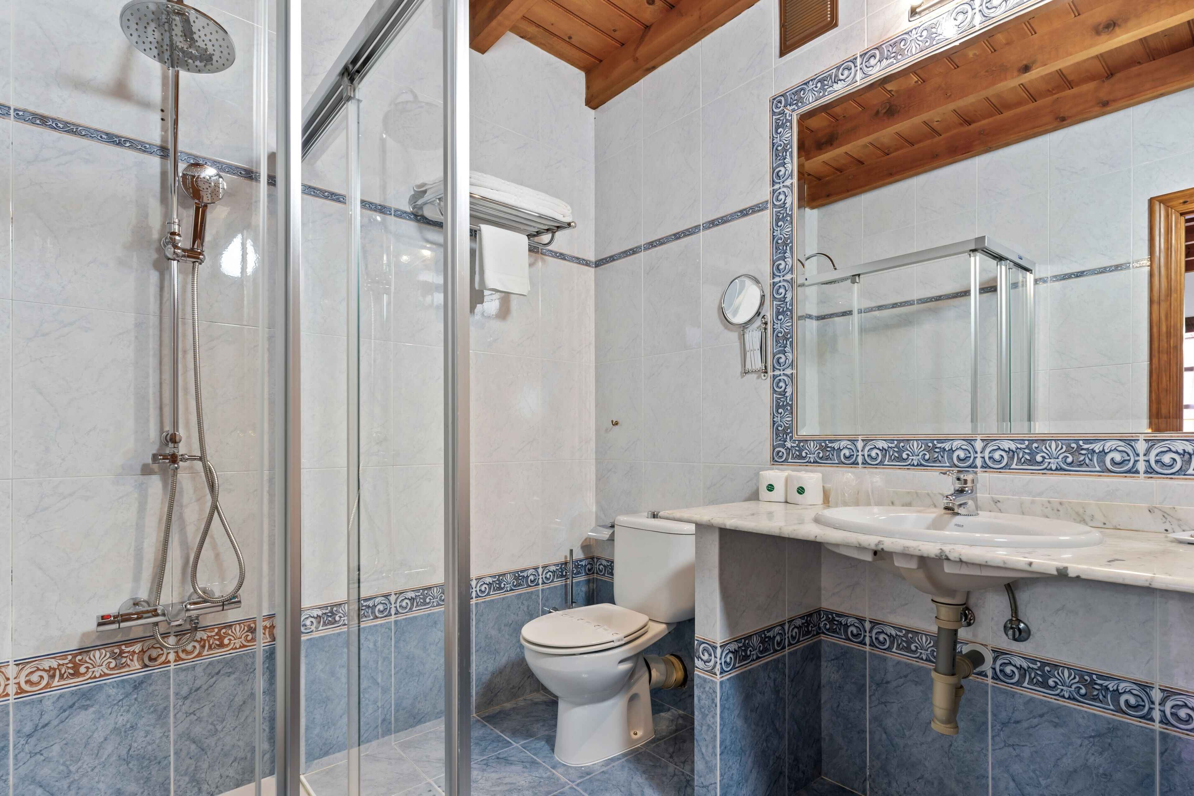 A bathroom with a glass shower enclosure, a toilet, and a sink with a mirror above it.