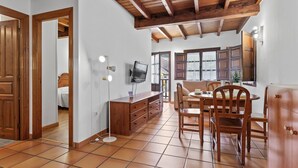 Une pièce spacieuse avec un plafond en bois, un coin repas comprenant une table et des chaises, un téléviseur fixé au mur et un lit dans la pièce adjacente.