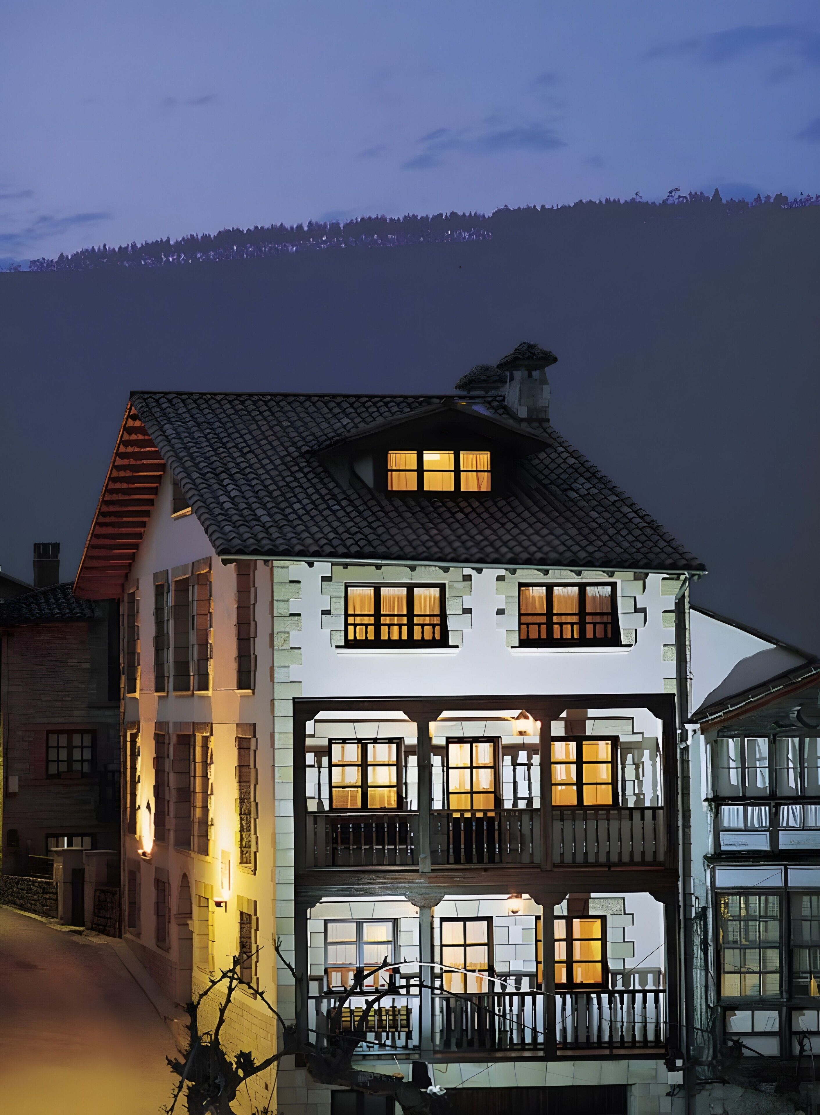 Un edificio a due piani con diverse finestre, un balcone e vista su una collina boscosa.