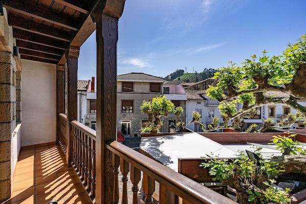 A balcony with a wooden railing overlooking a courtyard with potted plants and buildings.