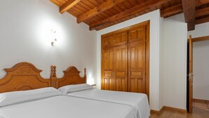 Une chambre avec deux lits, des têtes de lit en bois, une armoire et un plafond en bois.