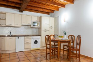 A compact kitchen with white cabinets, a microwave, a washing machine, and a dining area with wooden chairs and a table.
