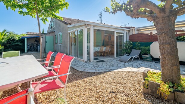 A covered patio area with a table and chairs, a tree, and a view of a house. - Holiday Home 'Hameau Du Soleil' with Shared Pool, Private Terrace and Private Garden (Vendres)