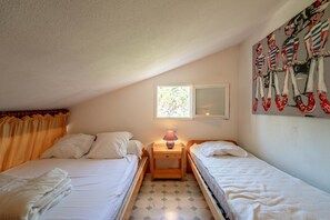 A bedroom with two single beds, a nightstand with a lamp, a window, and a wall painting.