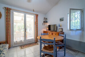 A room with a dining table, chairs, a sofa, a television, and a window with curtains.