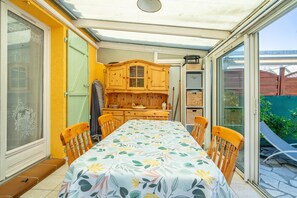 Un patio iluminado por el sol con una mesa y sillas, una puerta corrediza de vidrio y un armario de madera.