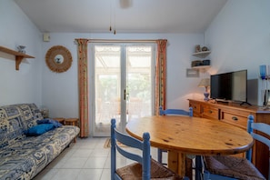 A living room with a sofa, a wooden dining table, chairs, a television, and a window with curtains.