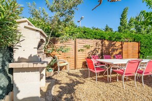 Un patio con una estructura de piedra, cerca de madera y sillas rojas alrededor de una mesa.