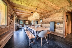 Interior de madeira com uma longa mesa de jantar, bancos e luminárias pendentes.