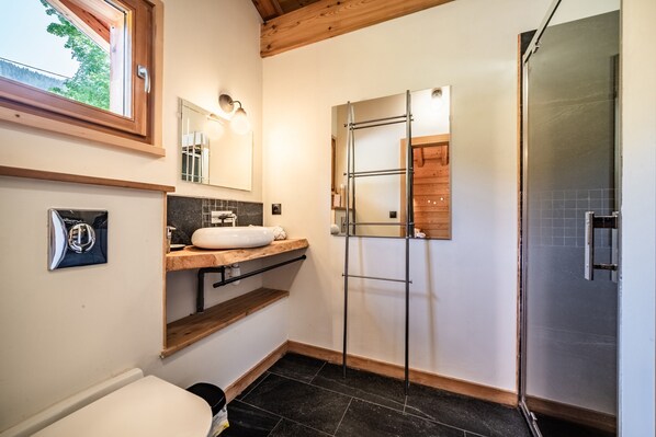 A bathroom with a wooden ceiling, a white sink, a mirror, a shower, and a window.