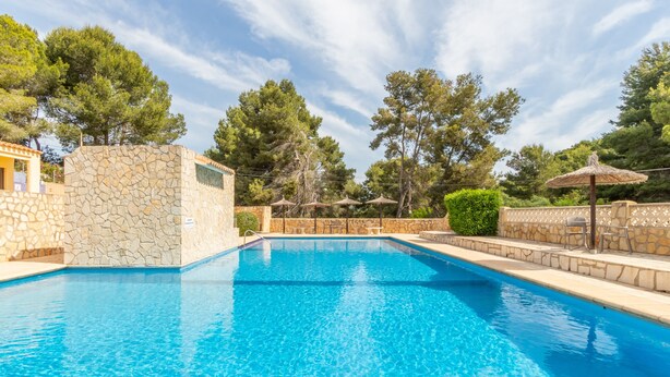 A swimming pool with stone walls, surrounded by trees and umbrellas. - Apartment 'Finca 9' with Shared Pool, Wi-Fi and Air Conditioning (Moraira)