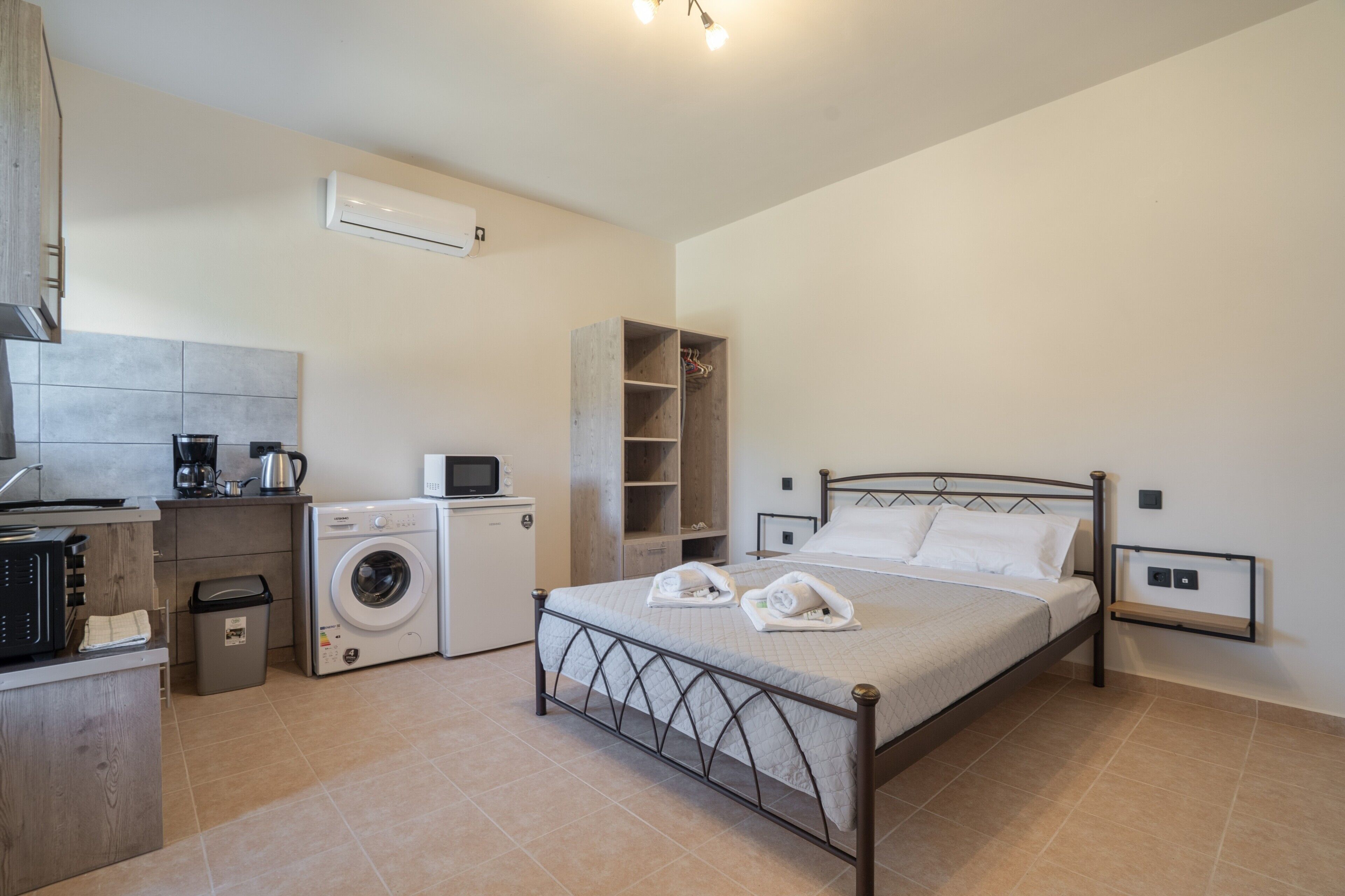 A bedroom with a bed, a washing machine, a microwave, and a small kitchenette.