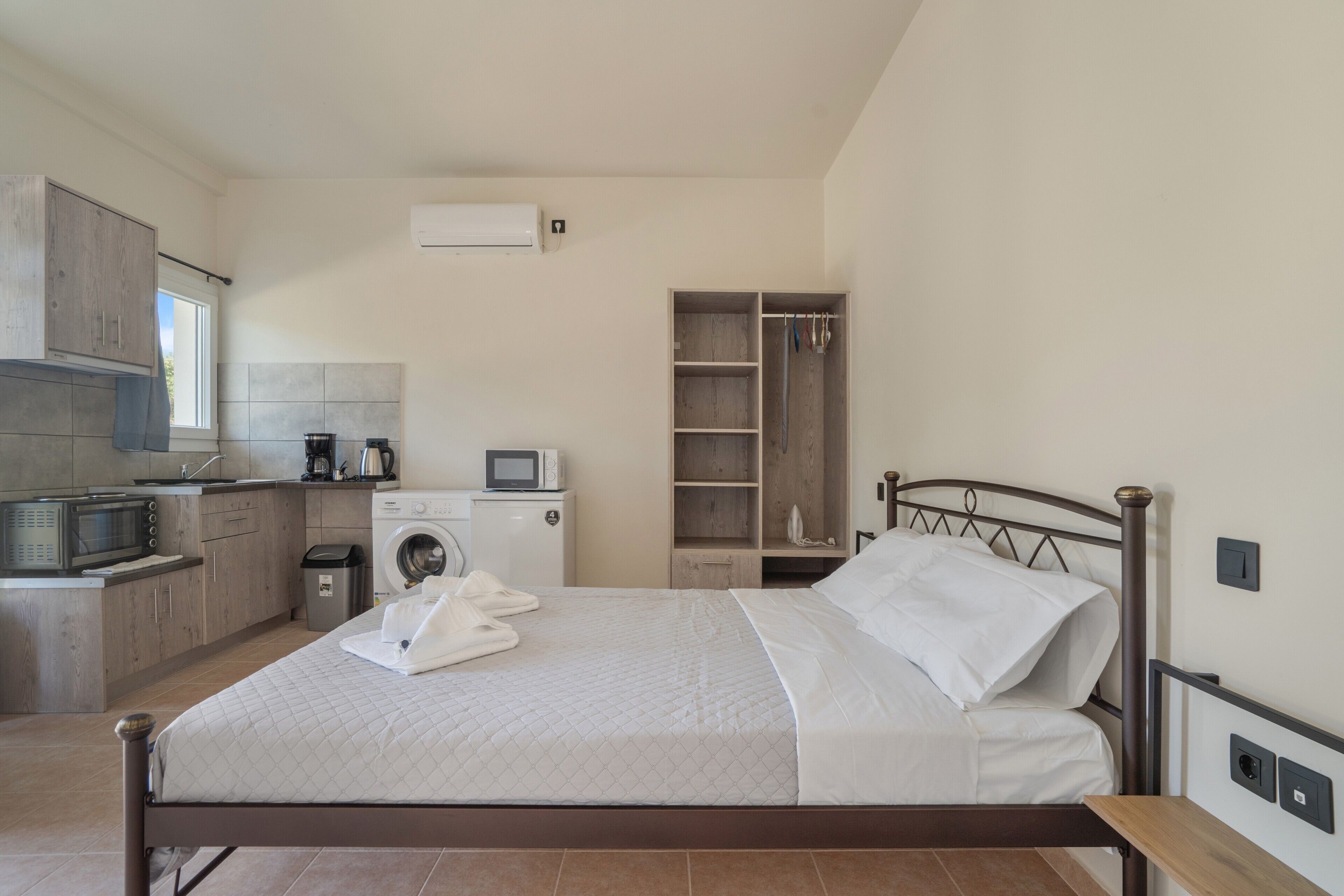 A bedroom with a bed, a built-in wardrobe, a washing machine, and a kitchenette.