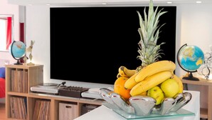 A fruit bowl on a table with a television and decorative items in the background.