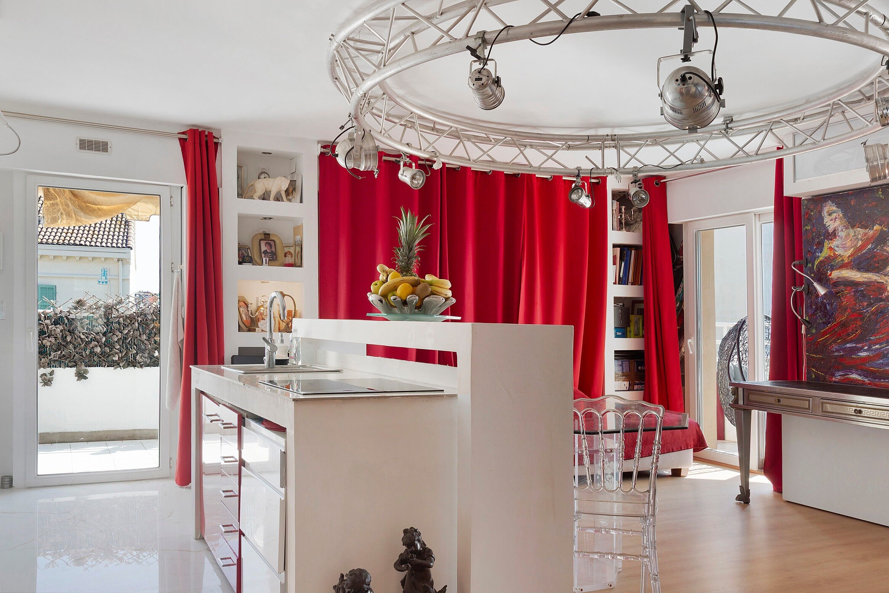 Un interno moderno con un'isola centrale, tende rosse e un soffitto con corpi illuminanti.