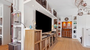 A modern living room with a flat-screen TV, wooden shelving, and a variety of decorative items. - Apartment 'Le Loft' with Mountain View, Wi-Fi and Air Conditioning (Cannes)