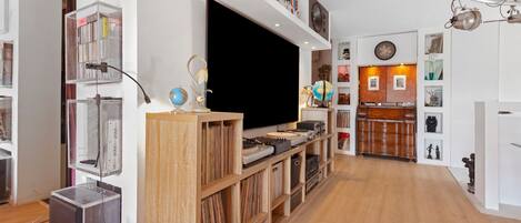 Un salon moderne doté d’un téléviseur à écran plat, d’étagères en bois et de divers objets décoratifs.