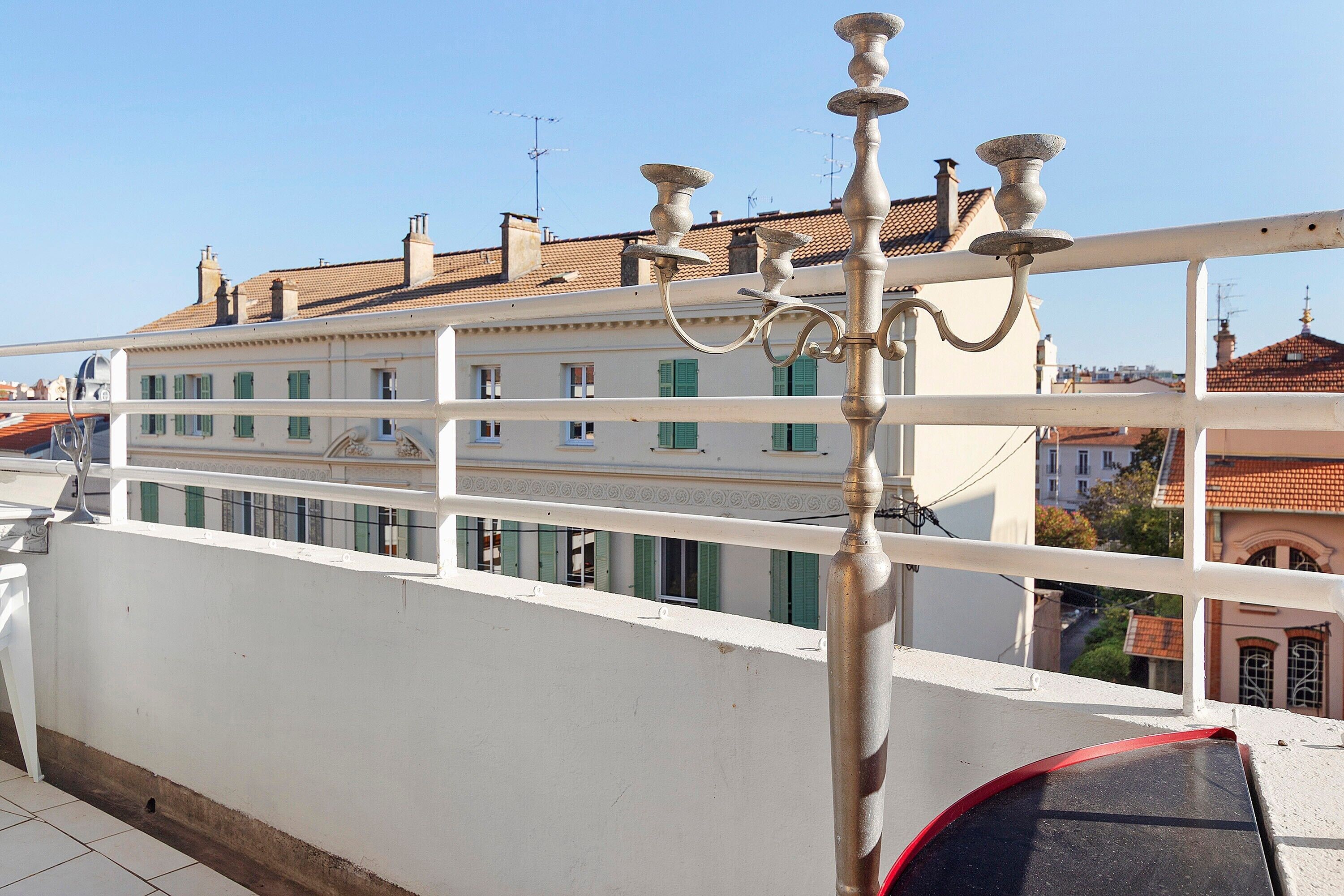 Un balcone con ringhiera bianca, un lampione in metallo e vista su un edificio con persiane verdi.