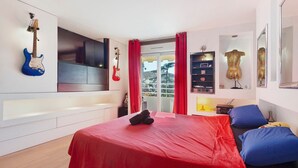 A bedroom with a bed, a TV, a guitar, and a window with curtains. - Apartment 'Le Loft' with Mountain View, Wi-Fi and Air Conditioning (Cannes)