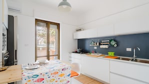 A modern kitchen with white cabinets, a dining table with a colorful tablecloth, and a window with a view of greenery. - Vacation Home 'Karma' with Sea View and Air Conditioning (Gallipoli)