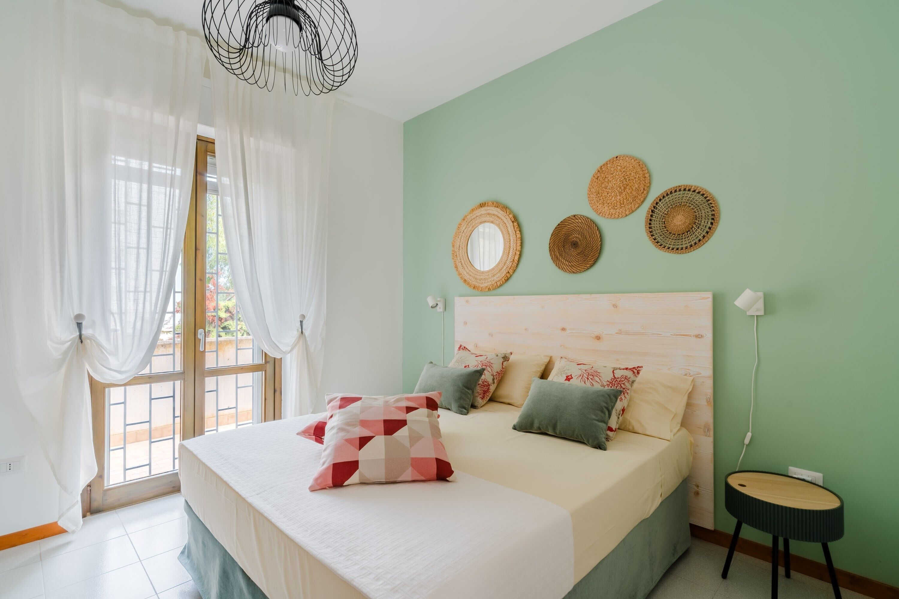 Une chambre à coucher avec un lit, des rideaux, un miroir fixé au mur et une table ronde.