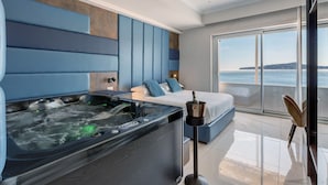 Ein modernes Hotelzimmer mit einer großen Badewanne, einem Bett mit blauer Bettwäsche und Meerblick.