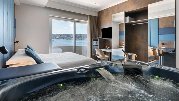 Ein modernes Hotelzimmer mit Bett, Schreibtisch, Stuhl, Fernseher und einer Whirlwanne.
